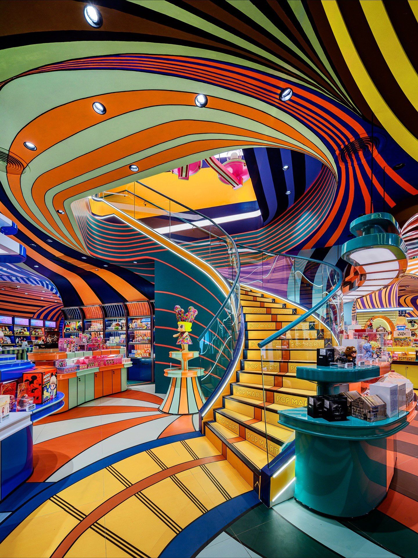 تصاویری از فضای داخلی فروشگاه پرچمدار برند پاپ مارت (POP MART) در مرکز خرید آیکون سیام بانکوک، که توسط استودیوی X+Living با طراحی مفهومی و الهام از نقوش معبد وات آرون تایلند اجرا شده و دارای فضای پیکسلی و کافه «داستان پریان» است.