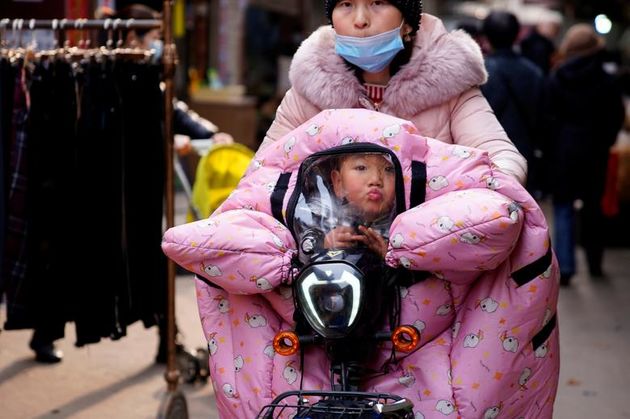 زنی با ماسک صورت با یک کودک در ووهان ، استان هوبئی ، چین دوچرخه سواری می کند. 